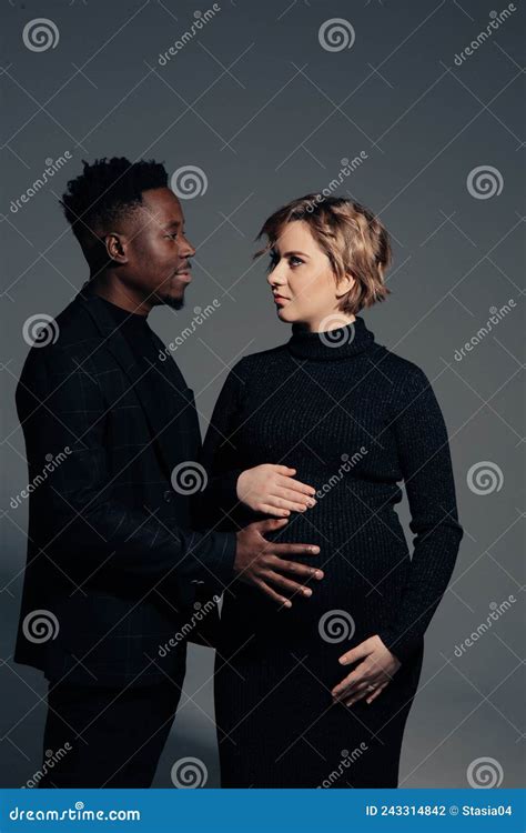 Young African Man And His Caucasian Pregnant Woman Stand Against Grey