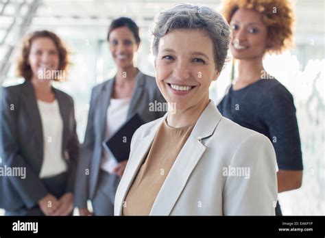 Portrait Of Smiling Mature Businesswoman With Office Team In Background