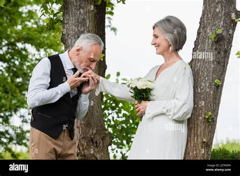 Mature Man In Formal Wear Kissing Hand Of Bride With Wedding Bouquet In