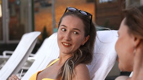 Happy Young Women Lying On Sunbeds By The Swimming Pool And Gossiping