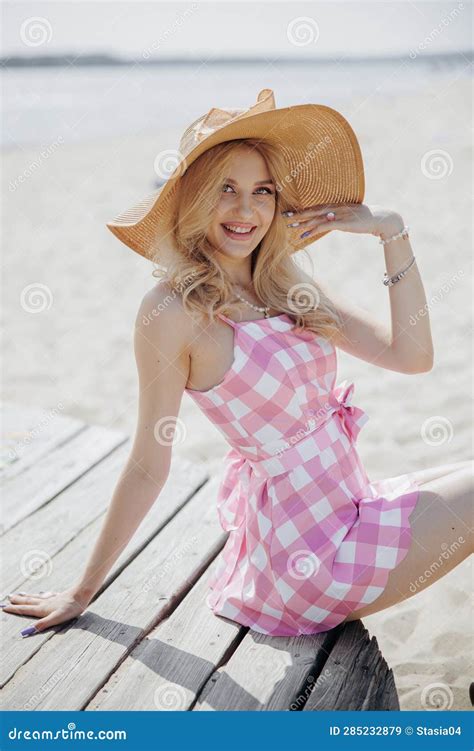 Young Smiling Blonde Girl Look Like A Barbie Doll In Pink Mini Dress And Wide Brim Hat Sitting