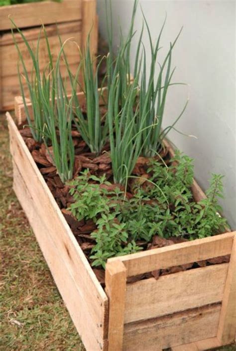 A Wooden Box Filled With Plants Next To A White Wall And Grass Growing