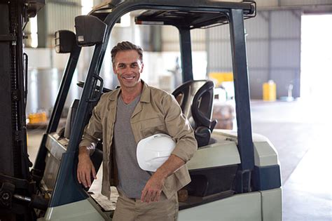 Portrait Of Happy Worker Standing Near Forklift In Oil Factory