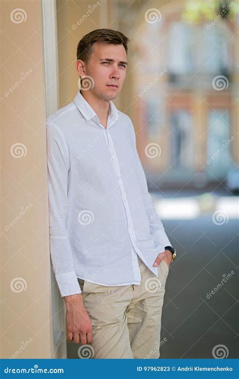 A Young Attractive Fellow In A White Shirt And Beige Pants Looks In The