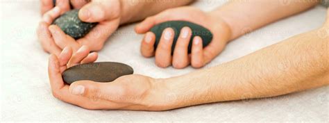 Four Hands Of Male Masseurs Holding Spa Stones On White Towel Top View