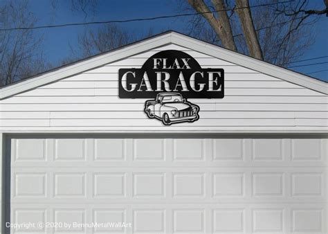 a garage sign on the side of a white building with trees in the back ground