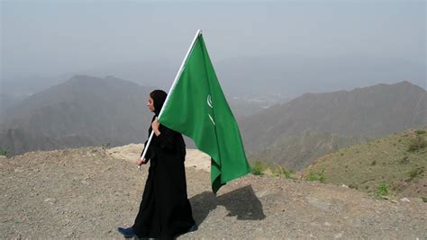 A Veiled Saudi Arabian Gulf Woman Holding The Flag Of The Kingdom Of