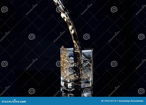 Whiskey Pouring Into Glass With Ice Isolated On Black Background Stock