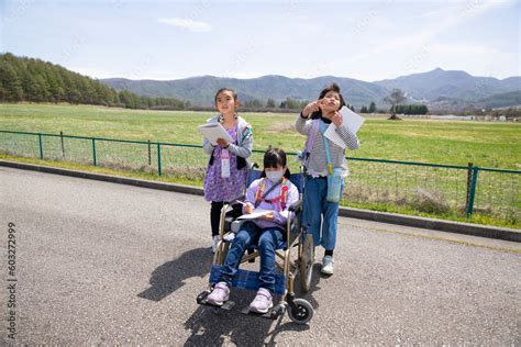 車いすに乗った女の子と学校の遠足に行く小学生の友達 Stock Foto Adobe Stock