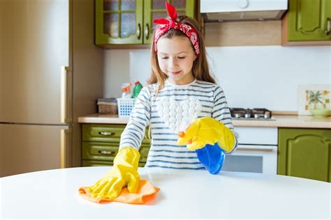 Menina criança positiva faz a limpeza da mesa da cozinha o adolescente