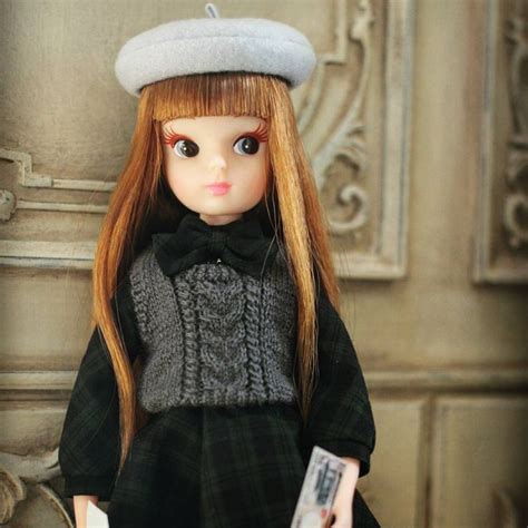 A Doll With Long Red Hair Wearing A Black Dress And Gray Hat Holding A