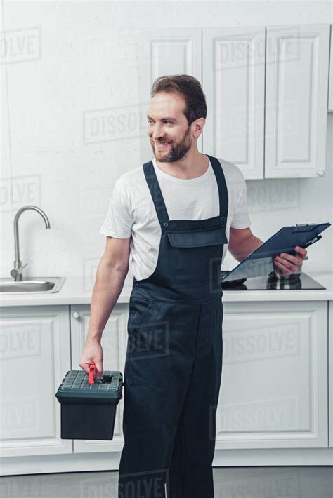 Happy Adult Repairman In Working Overall Holding Toolbox And Clipboard