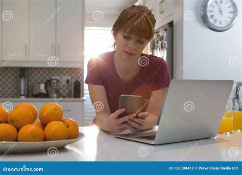 Mulher Que Usa O Telefone Celular Na Cozinha Foto De Stock Imagem De