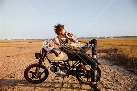 Adventurous Man Resting On His Motorcycle In The Desert And Hydrating