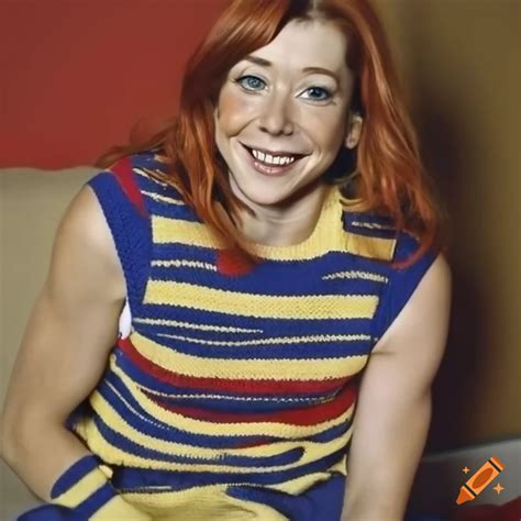 Smiling Alyson Hannigan Sitting On A Bed Wearing A Striped Sweater Vest