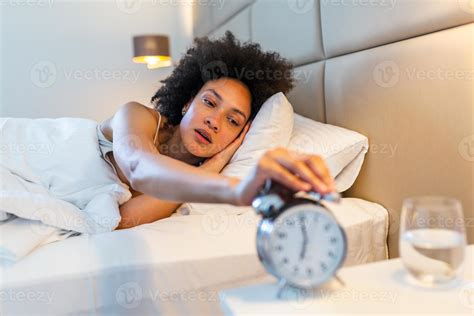 Woman Lying In Bed Turning Off An Alarm Clock In The Morning At 7am