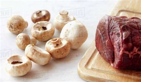 Raw Beef Tenderloin On A Wooden Cutting Board With Raw Mushrooms