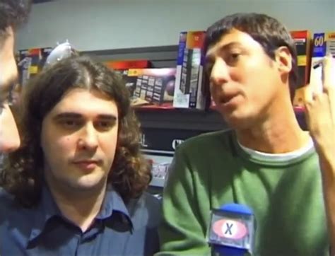 Two Men Are Talking To Each Other In Front Of A Microphone And Bookshelves