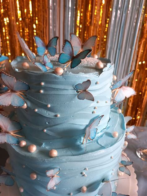 A Three Tiered Blue Cake With Butterflies On The Top And Pearls Around The Edges