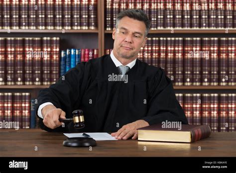 Confident Mature Male Judge Striking The Gavel At Table Against