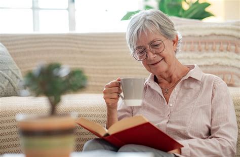 Belle femme senior assise sur le sol à la maison en lisant un livre