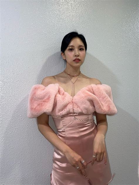 A Woman In A Pink Dress Standing Next To A White Wall And Looking At