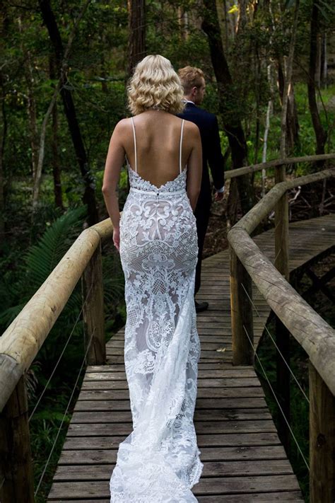 A Woman In A Wedding Dress Walking Across A Wooden Bridge With Her Back