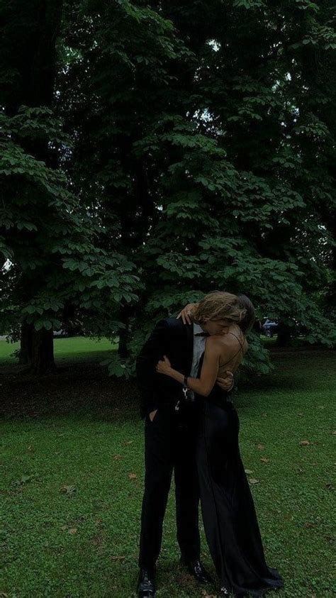 A Man And Woman Are Kissing In Front Of Some Trees On A Grassy Field