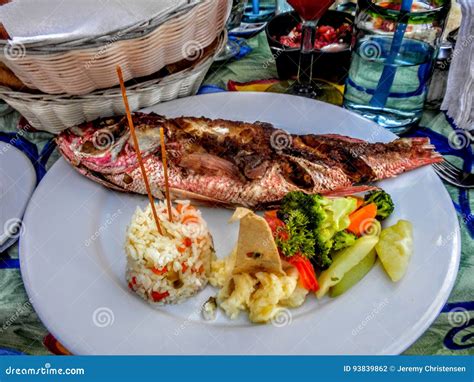 Fried Whole Fish With Rice And Vegetables On Plate At Lunch Table