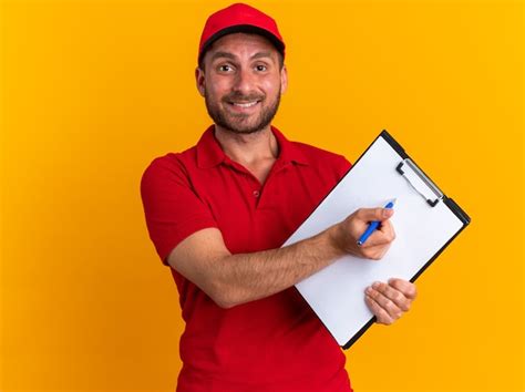 Sonriente joven repartidor caucásico en uniforme rojo y gorra mirando a