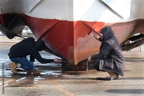 Men painting hull of a fishing boat out of the water. Stock Photo ...