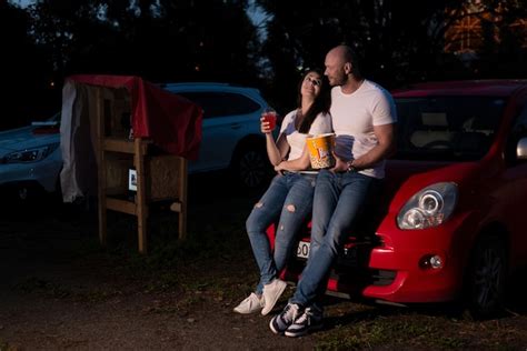 Premium Photo | Couple with popcorn standing at the car while watching a movie at drive in ...