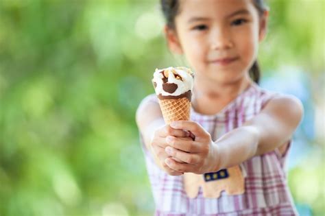 La Pequeña Muchacha Asiática Linda Del Niño Está Comiendo El Cono Delicioso Del Helado Con