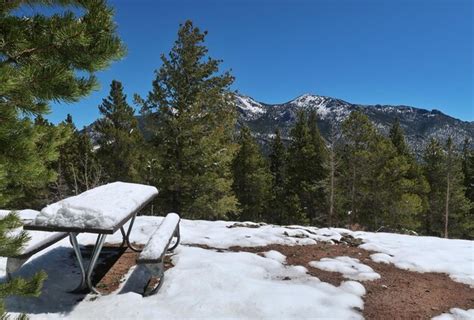 Mesa de piquenique coberta de árvores de neve e montanhas ao fundo nas