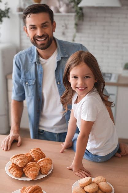 Retrato De Padre E Hija Sonrientes Sentados En La Mesa De La Cocina Y Mirando A La Cámara Foto