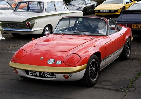 An Old Red Sports Car Parked In A Parking Lot With Other Cars Around