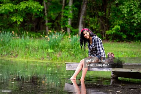 Beautiful Brunette Woman Sitting On Dock Feet In The Water High Res