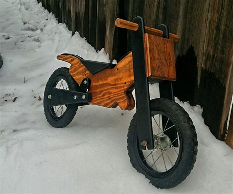 A Small Wooden Bike Sitting In The Snow Next To A Fence And Wood Slats