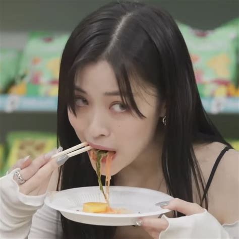 A Woman Eating Food With Chopsticks In Her Mouth While Holding A White