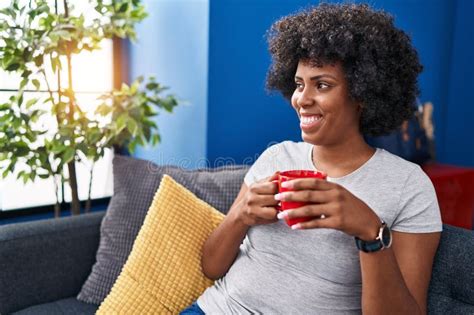 African American Woman Drinking Coffee Sitting On Sofa At Home Stock