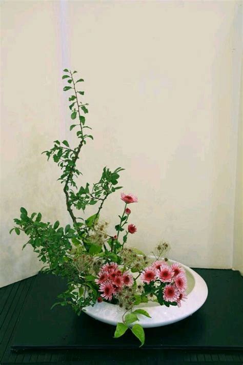 A White Plate With Pink Flowers And Greenery In It Sitting On A Black Table