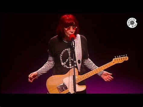 A Man With Red Hair And Glasses Holding A Guitar In Front Of A