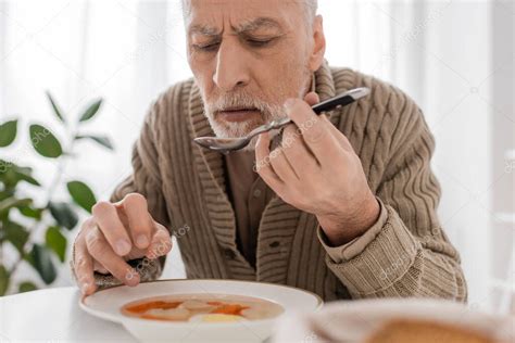 Senior Bearded Man Suffering From Parkinsonism And Holding Spoon In