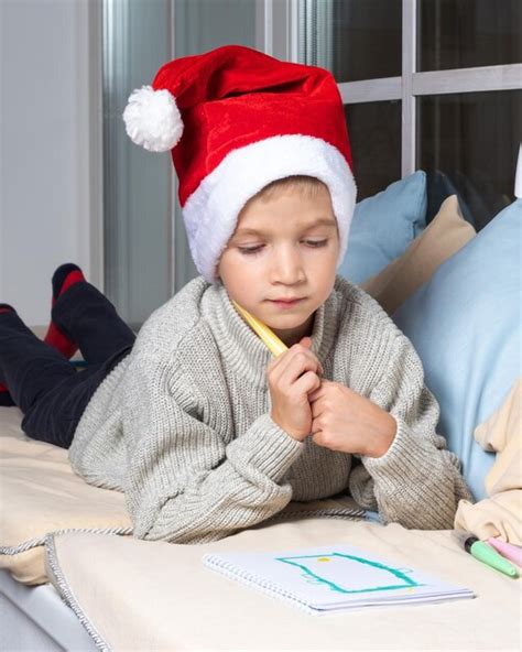 Un enfant sérieux et concentré dans un bonnet de Noel écrit une liste