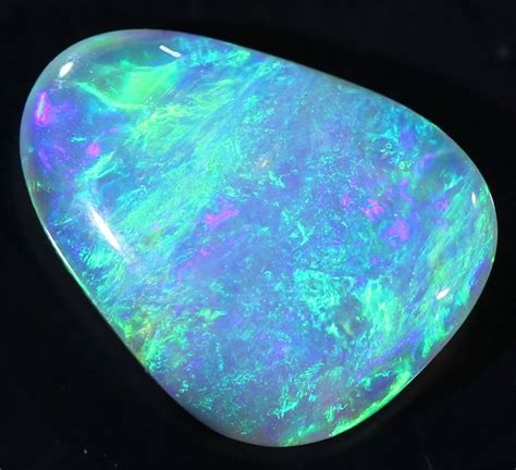 An Opalite Stone Sitting On Top Of A Black Surface With Green And Blue