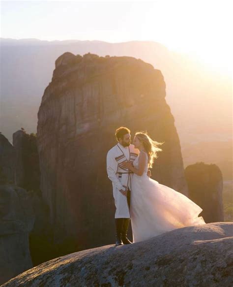 A Bride And Groom Standing On Top Of A Rock Formation In Front Of The Sun