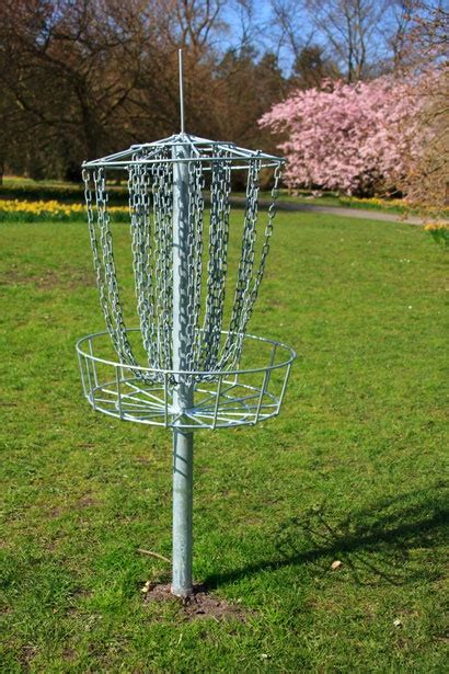 A Frisbee Golf Cage In The Middle Of A Grassy Area With Trees And Flowers Behind It