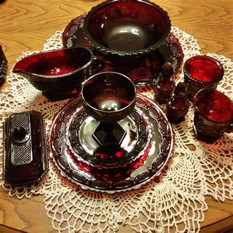 A Table Topped With Lots Of Red Glass Dishes And Cups On Top Of A Doily