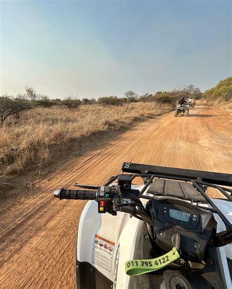 Two Atvs Driving Down A Dirt Road In The Middle Of Dry Grass And Brush