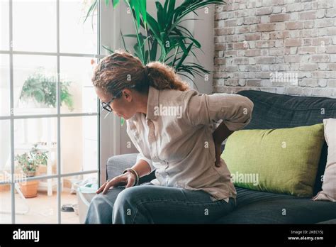 Unhealthy curly woman sit on couch at home stretching suffering from ...